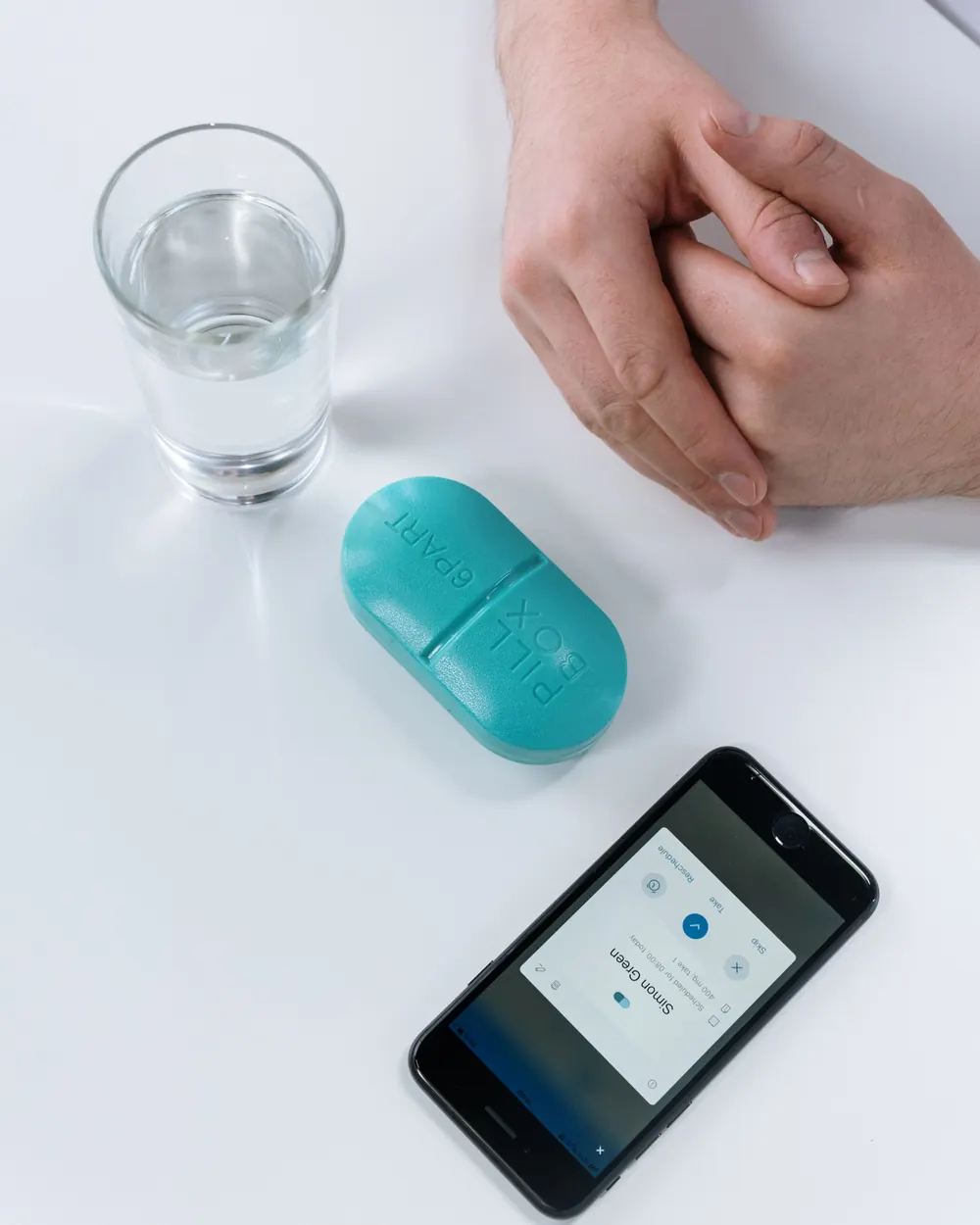 A pill case, a glass of water and a phone showing a medication reminder app