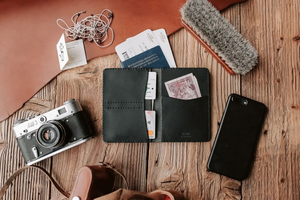 Traveller essentials including a wallet, camera and phone on a wooden table