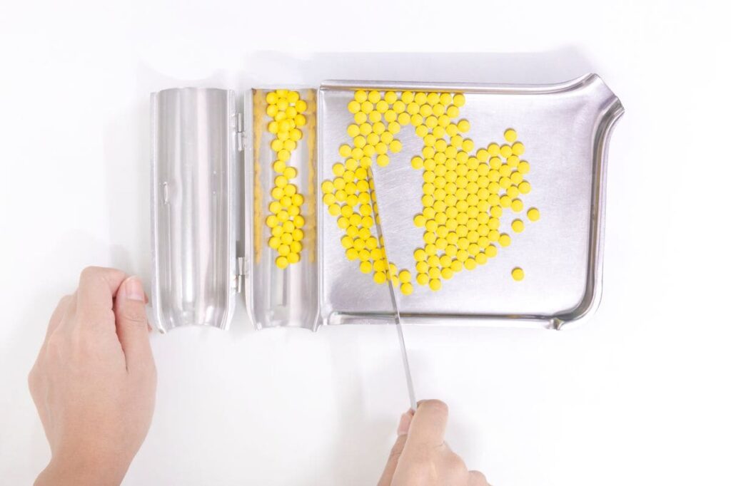 Pharmacy technician sorting pills on a stainless steel tray