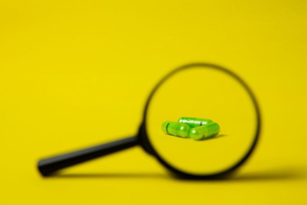 Magnifying glass beside a heap of green pills