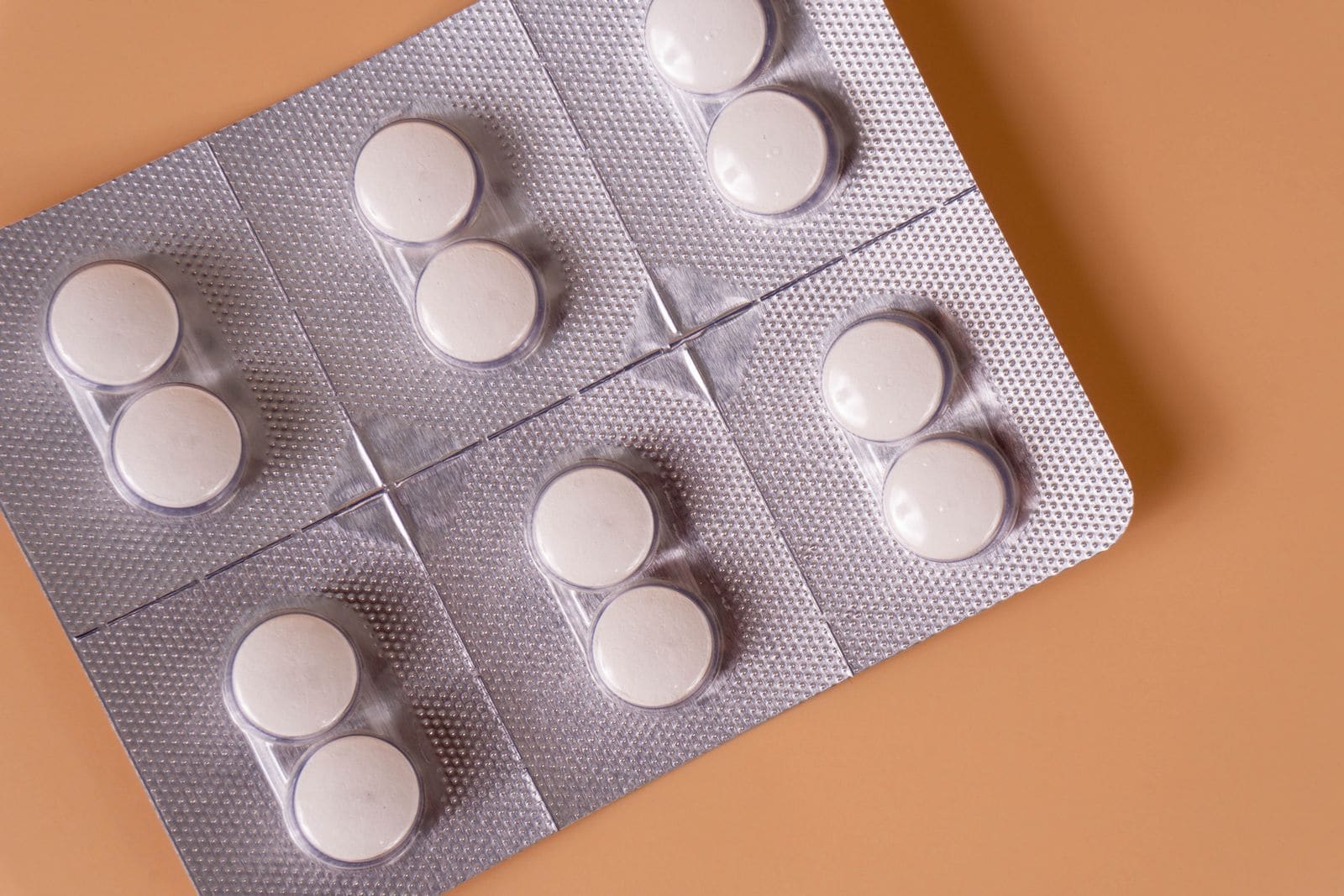 White pills in a blister pack on a peach background
