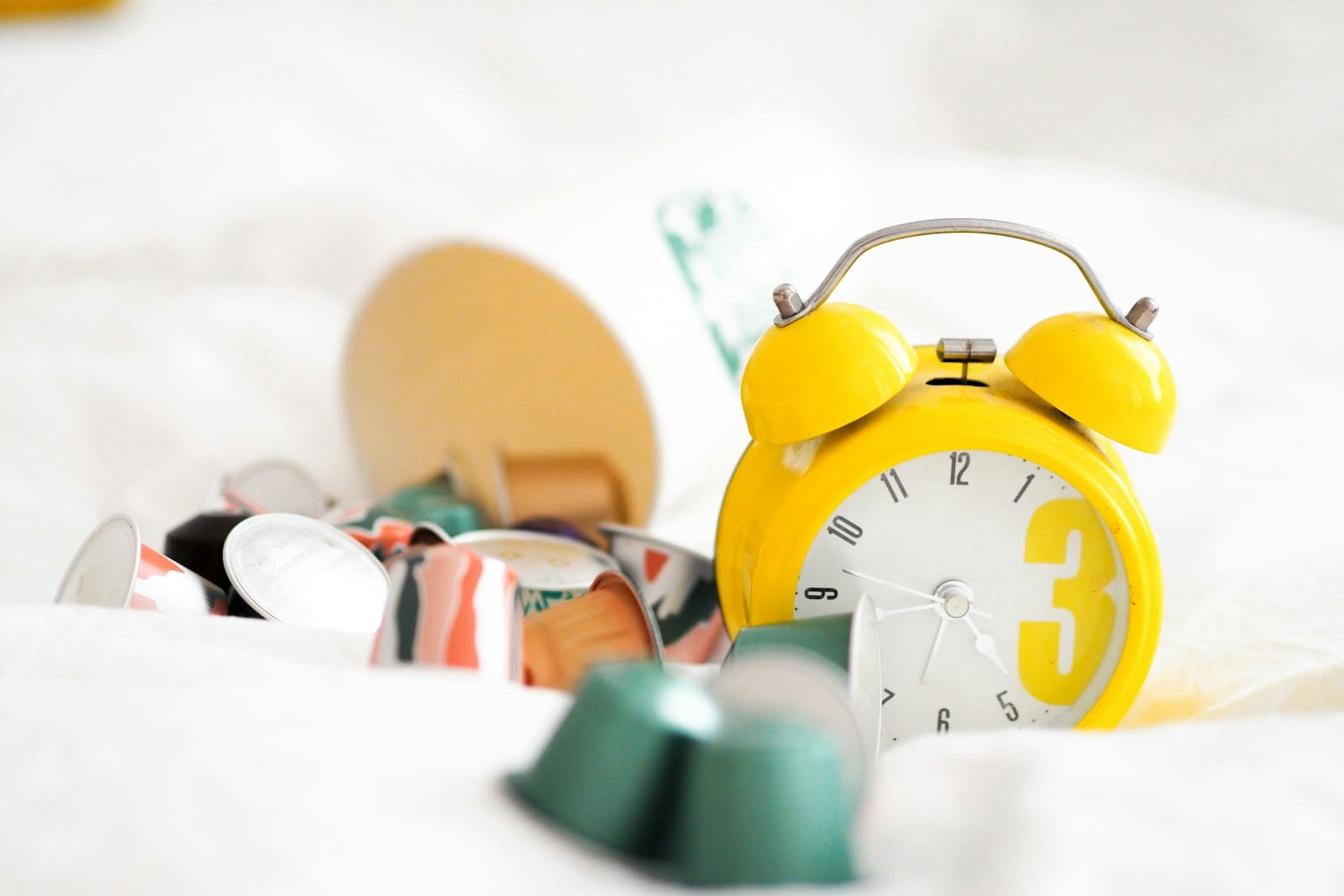 Yellow alarm clock beside a cup of spilled pills and capsules