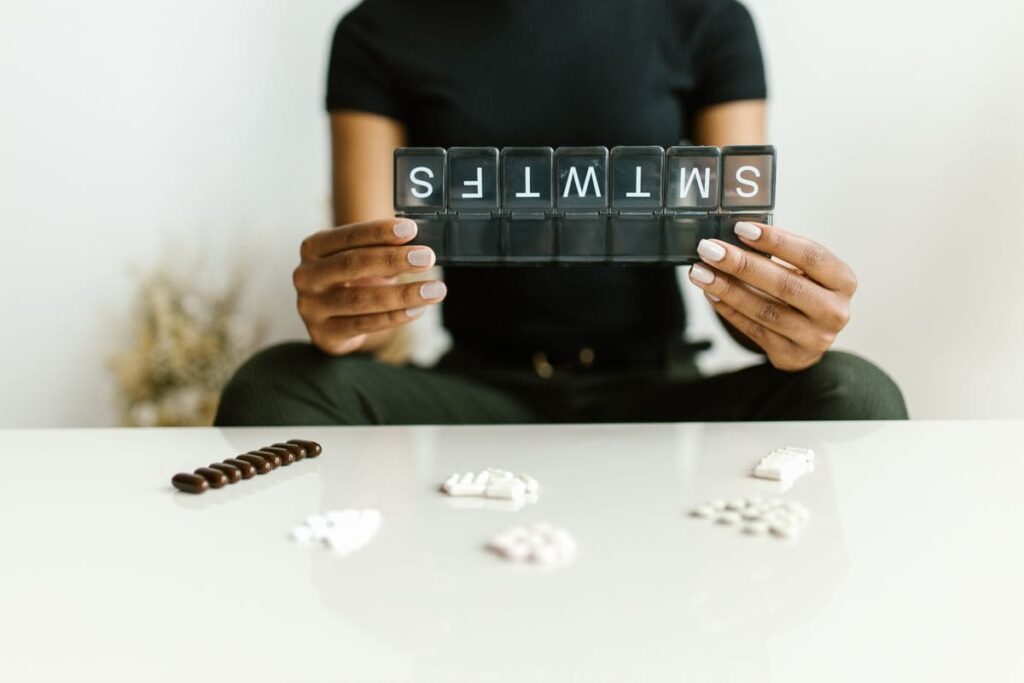 Person holding a weekly pill organiser above a table of pills