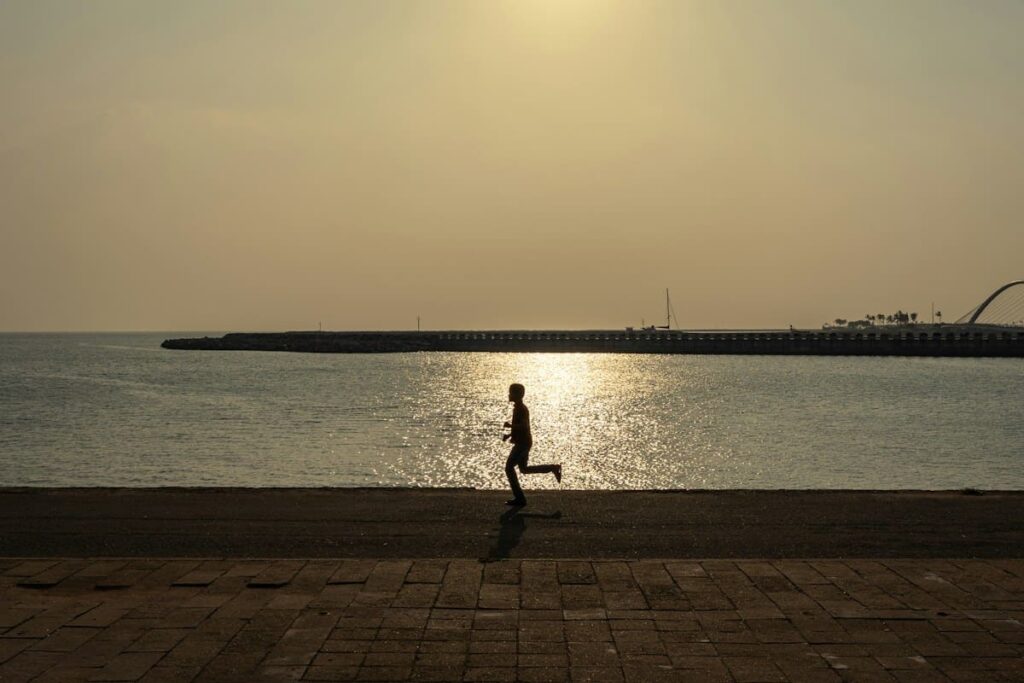 Silhouette of a person running along the waterfront at sunset