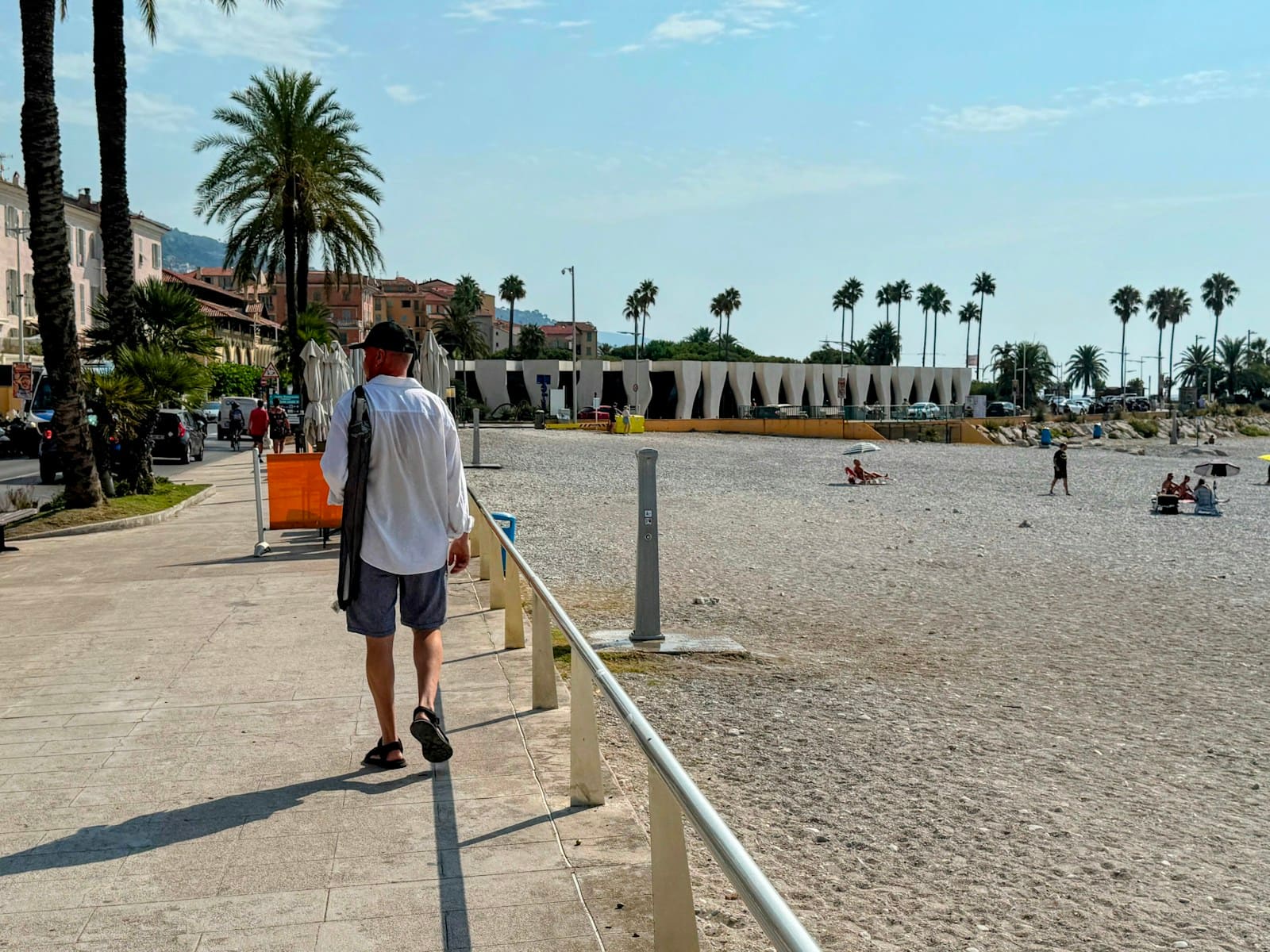 Man walking along a sunny beach promenade lined with palm trees
