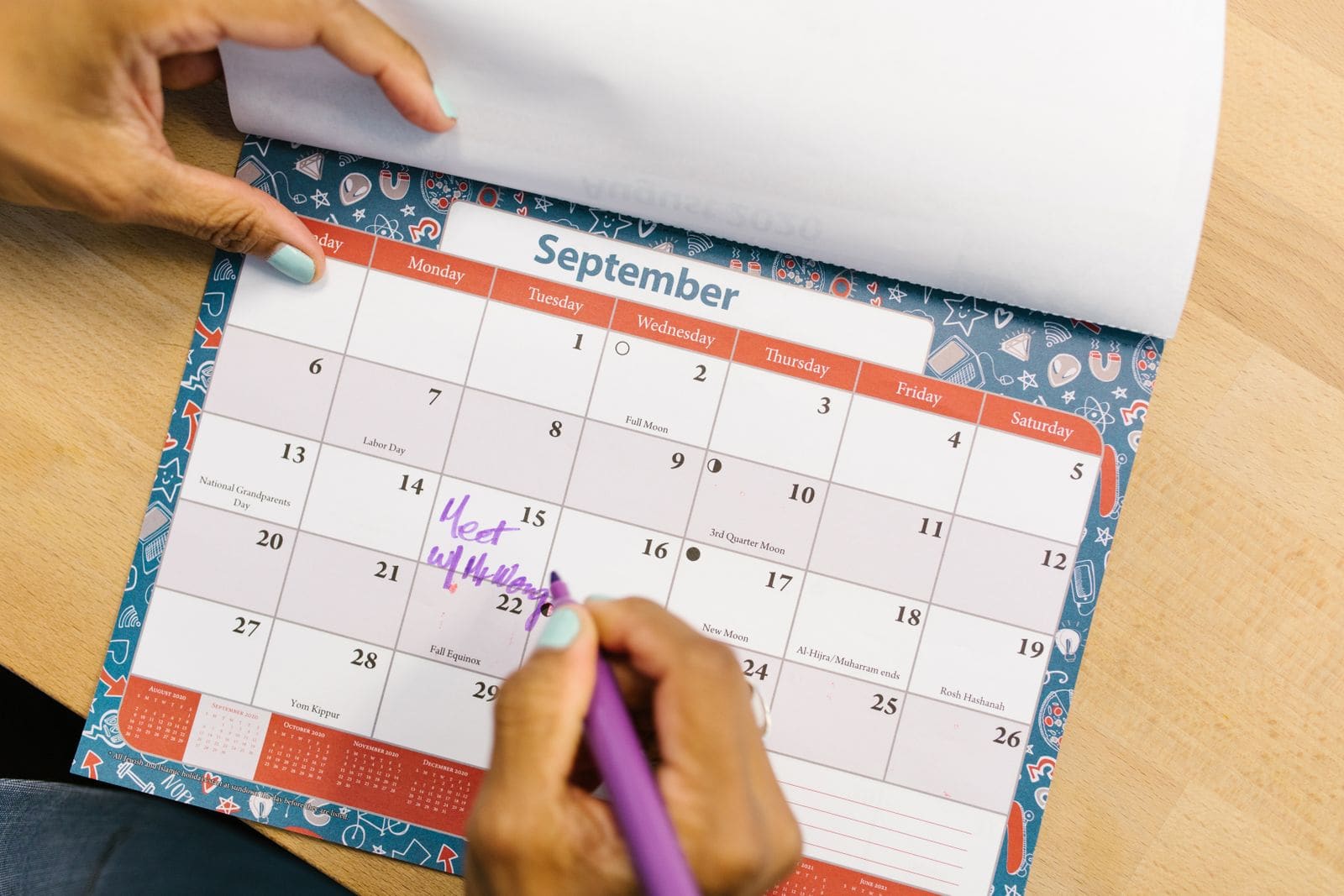 Hand marking dates on a calendar with a purple pen
