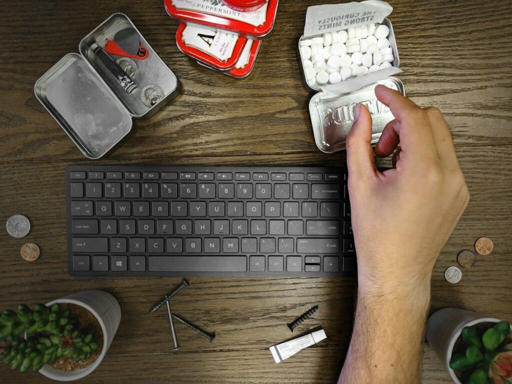 Hand opening a small pill tin next to a keyboard