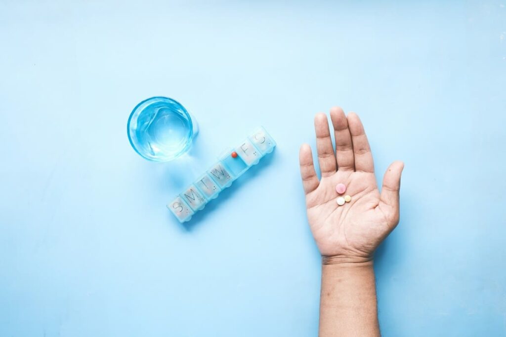 Open hand holding a pill beside a pill organiser