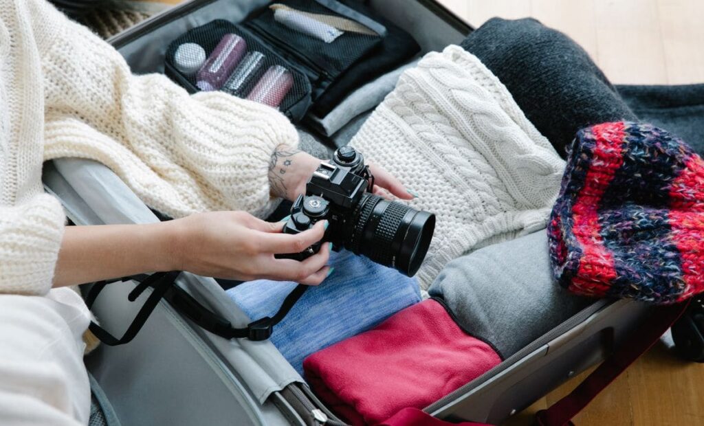 Packing clothes and a camera into a suitcase before a trip