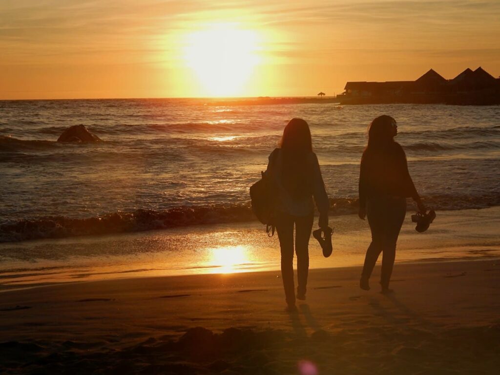Silhouettes of two women walking on a beach at sunset